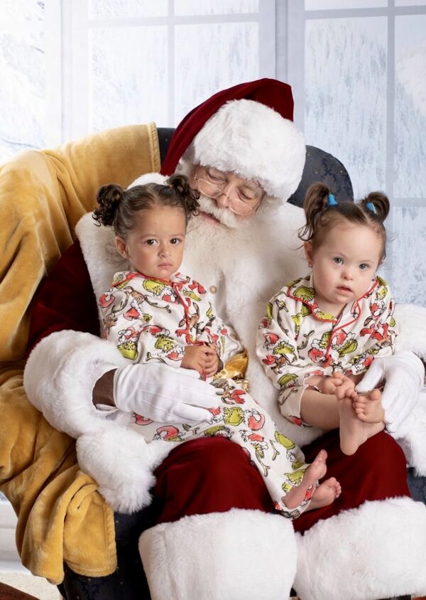 Twin toddlers in matching outfits on Santa Ray’s lap