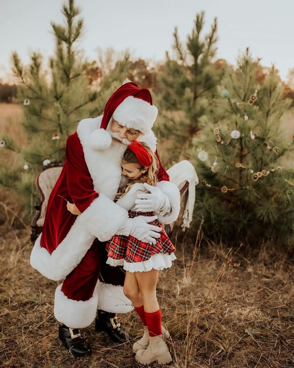 A little girl hugging Santa Ray among young pine trees