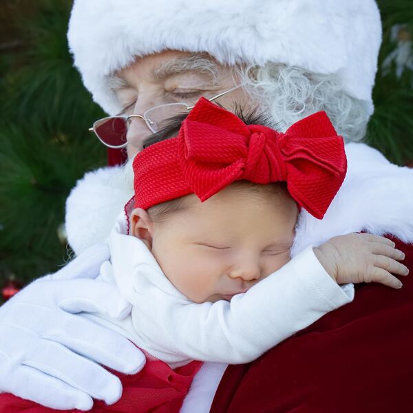 A sleeping baby with a red bow cradled by Santa Ray