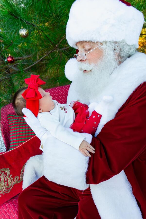 Santa Ray holding a baby beside a Christmas tree