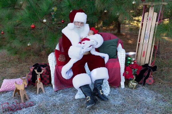 Santa Ray in a red armchair outdoors beside a wooden sled