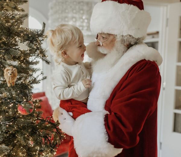 A young child on Santa Ray’s lap beside a Christmas tree