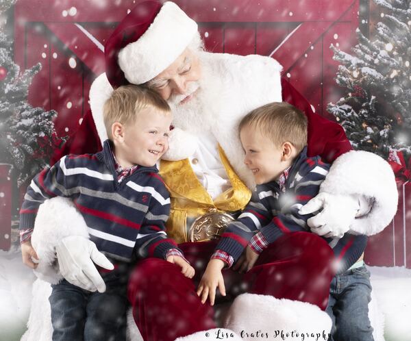 Two little boys on Santa Ray’s lap in a snowy red set